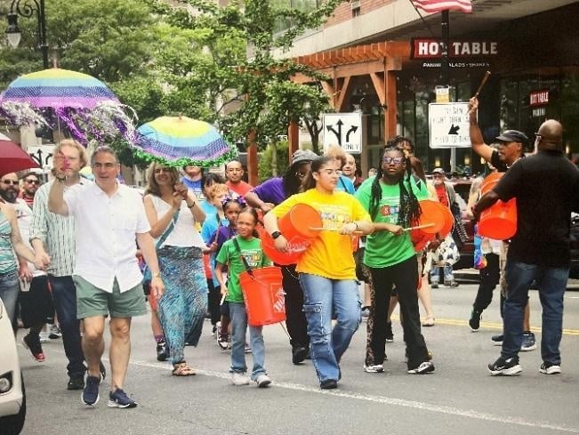 A multigenerational parade with colorful umbrellas and percussion instruments