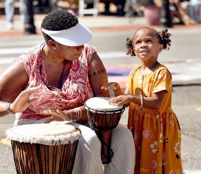 An adult and child playing hand drums together at the festival